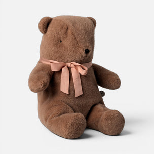 A brown plush Maileg teddy bear sitting down with a dusty pink satin bow tied around its neck, set against a plain light gray background.
