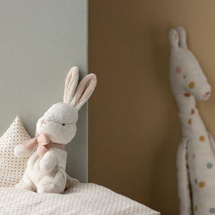 Stuffed rabbit toy on a bed with a neutral wall background