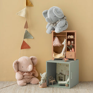 Two plush elephants and a small dollhouse on a beige carpet with a beige wall.