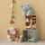 Two plush elephants and a small dollhouse on a beige carpet with a beige wall.