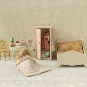 Miniature bedroom set with bed, chair, and wardrobe against a patterned wall.