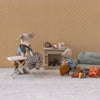 Two Maileg toy mice in a living room setting with furniture and accessories on a beige patterned wall background.