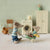 Two toy Maileg mice in a miniature room with a washing machine and furniture.
