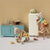 Miniature kitchen scene with toy animals and furniture against a patterned wall.