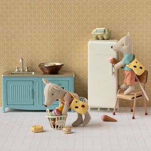 Miniature kitchen scene with toy animals and furniture against a patterned wall.