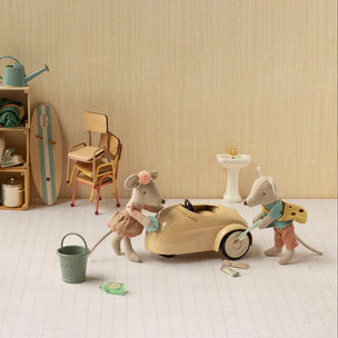 A styled miniature toy scene featuring two mouse figurines playing with a beige toy car, alongside a small bucket, lanterns, a chair, shelving, and other vintage-inspired accessories against a cream striped backdrop.