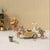 A styled miniature toy scene featuring two mouse figurines playing with a beige toy car, alongside a small bucket, lanterns, a chair, shelving, and other vintage-inspired accessories against a cream striped backdrop.