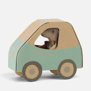 A small Maileg mouse dressed as a driver inside a handmade cardboard car. The car features a sage green side panel, a natural brown cardboard roof and wheels, and a small embroidered patch on the side.