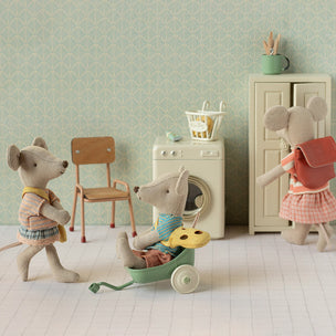 Three toy Maileg mice in a room with a chair, washing machine, and cabinet.