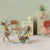 Three toy Maileg mice in a room with a chair, washing machine, and cabinet.
