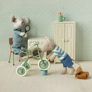 Two toy maileg mice in a room with a tricycle and other items.