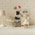 Two toy Maileg  mice in a room with a lamp, table, and mirror.