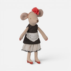 A plush Maileg mouse doll with beige fabric body and ears, wearing a dark brown dress with a white apron panel, a red flower headband, and red shoes, photographed on a clean light gray background.