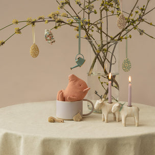 Decorative table setting with a pink plush toy, candles, and Easter decorations on a beige background.
