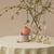 Decorative table setting with a pink plush toy, candles, and Easter decorations on a beige background.