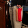 Person wearing beige pants with a red and white pouch on a dark background