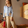 Person wearing a patterned outfit standing in a bedroom with colorful pillows and furniture.