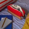 Red pencil case with a pen and notebook on a bed