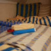 Small pouch with a red pull tab on a bed with striped bedding and pillows.
