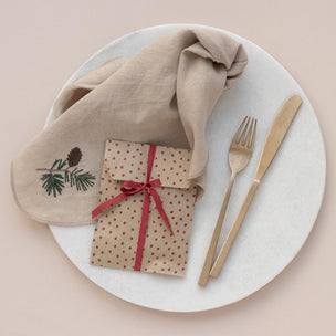 Plated setting with a folded napkin, wrapped gift, fork, and knife on a beige background