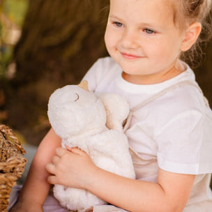 Young girl in a white dress holding a teddy bear outdoors.