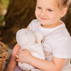 Young girl in a white dress holding a teddy bear outdoors.