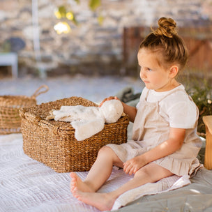 Young girl sitting on a blanket outdoors with a basket and wooden stool.