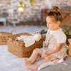 Young girl sitting on a blanket outdoors with a basket and wooden stool.