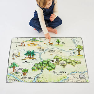 Child playing with a map of 100 Acre Wood on a white floor