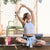 Woman practicing yoga outdoors on a wooden deck with a pink water bottle nearby.
