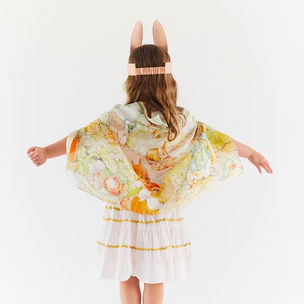 Person wearing a white dress with a colorful floral cape and bunny ears on a light gray background