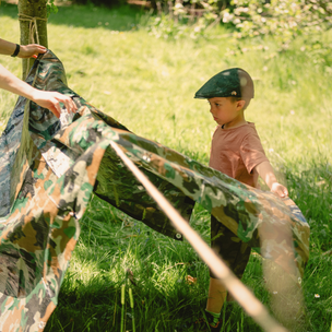 Child playing with a camouflage tent in a grassy outdoor setting