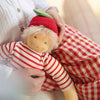 Child holding a small doll dressed in red and white with a green hat, sitting on a red and white checkered blanket.