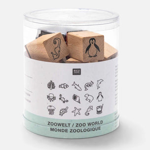 A clear cylindrical plastic container holding several small wooden animal stamps with black engraved outlines, wrapped in a white paper label that reads 'RICO DESIGN' and 'ZOOWELT / ZOO WORLD / MONDE ZOOLOGIQUE'.