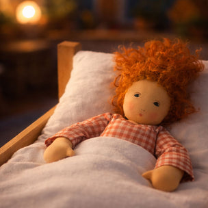 Toy doll with red hair lying on a bed in a softly lit room