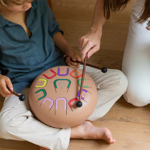 Two children playing with a colorful drum on a wooden floor.