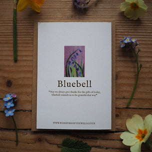 Card with bluebell design and text on a wooden surface with flowers