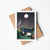 Greeting card with tent under a moonlit sky, placed on a white surface with a brown envelope.