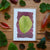 Card with pressed leaf design surrounded by real leaves on a wooden surface