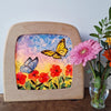 Decorative piece with butterflies and flowers in a wooden frame, next to a vase with flowers.