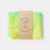 Folded green and yellow fabric with a brown card labeled 'Laura's Play Cotton' on a white background