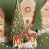 Wooden reindeer figures with a decorated Christmas tree and houses in the background.
