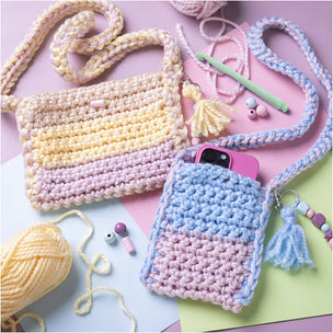 Crocheted bags and phone case with yarn and tools on a colorful background