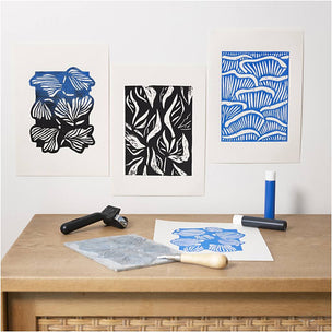Wooden table with printmaking tools and framed artwork on a white wall