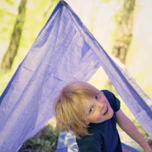 Child playing under a blue canopy in a forest setting
