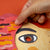 Hand interacting with a colorful paper cutout of a face on an orange background