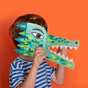Child holding a green paper crocodile mask against an orange background