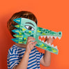 Child holding a green paper crocodile mask against an orange background