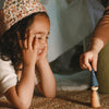 Grapat Avent Calendar 2025  Child wearing a floral crown playing with a wooden toy on a carpeted floor.