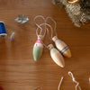 Three wooden ornaments on a wooden surface with thread and fabric scraps.